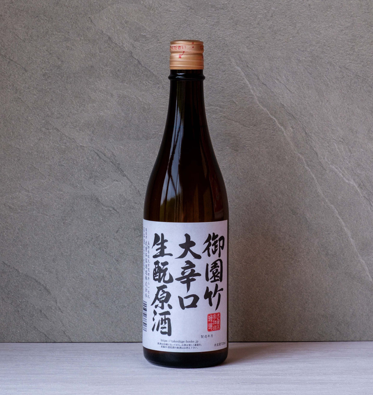 A single bottle of Japanese sake (shuizake) with a white label and black calligraphy, standing on a light gray surface against a textured gray background.